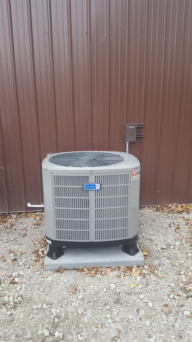 American Standard air conditioner set on a level pad outside a shop